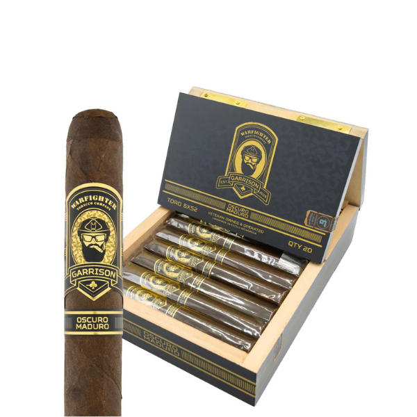 An open box of Warfighter Tobacco’s .50 Cal Garrison Oscuro Maduro Robusto cigars displays several full-bodied sticks, with one cigar shown in close-up to highlight its detailed label.