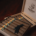 A wooden box of Foundation Olmec Claro Robusto cigars, each with a yellow and black circular band, with the brand logo branded on the inside of the lid.