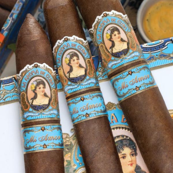Close-up of three brown La Aroma De Cuba Mi Amor Belicoso cigars with ornate blue and gold bands featuring a woman's portrait, showcasing these premium Nicaraguan cigars from La Aroma De Cuba.