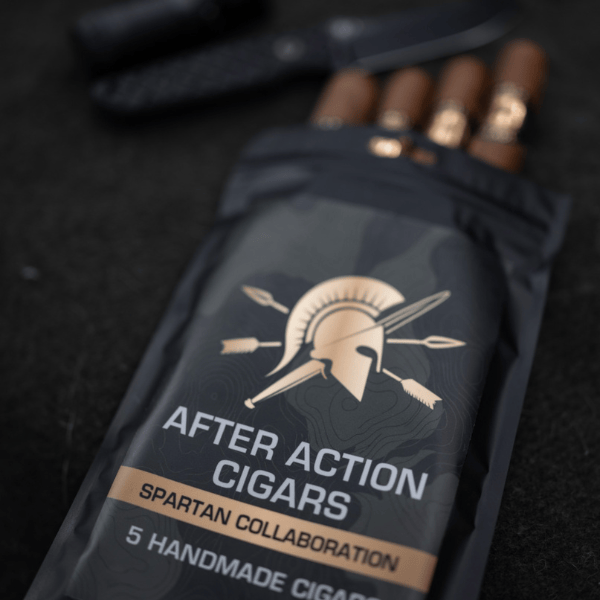 A black pouch labeled “After Action Cigars Spartan Collaboration” contains five limited-edition Spartan Blades Habano Toro cigars, with a Spartan Blades knife and another object in the background on a dark surface.