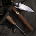 A closed folding knife, a Spartan Blades Habano Toro brown limited-edition cigar, and a fire starter with striker sit atop an olive-green backpack.