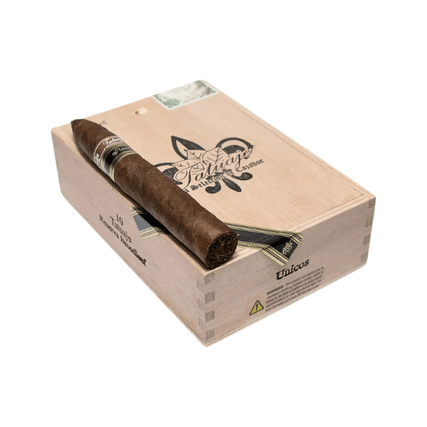 A single Tatuaje Reserva Broadleaf Unicos cigar rests on a closed wooden cigar box adorned with decorative branding and a small warning label on the side.